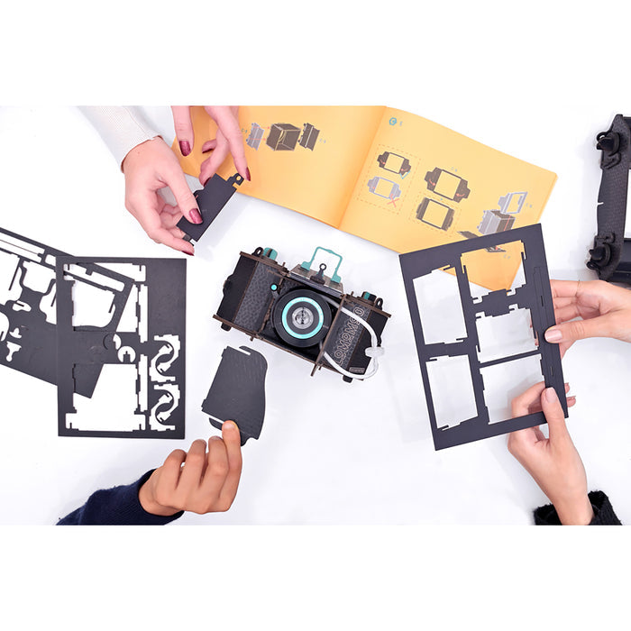 Hands holding a paper model of a camera with cut-out pieces on a white background